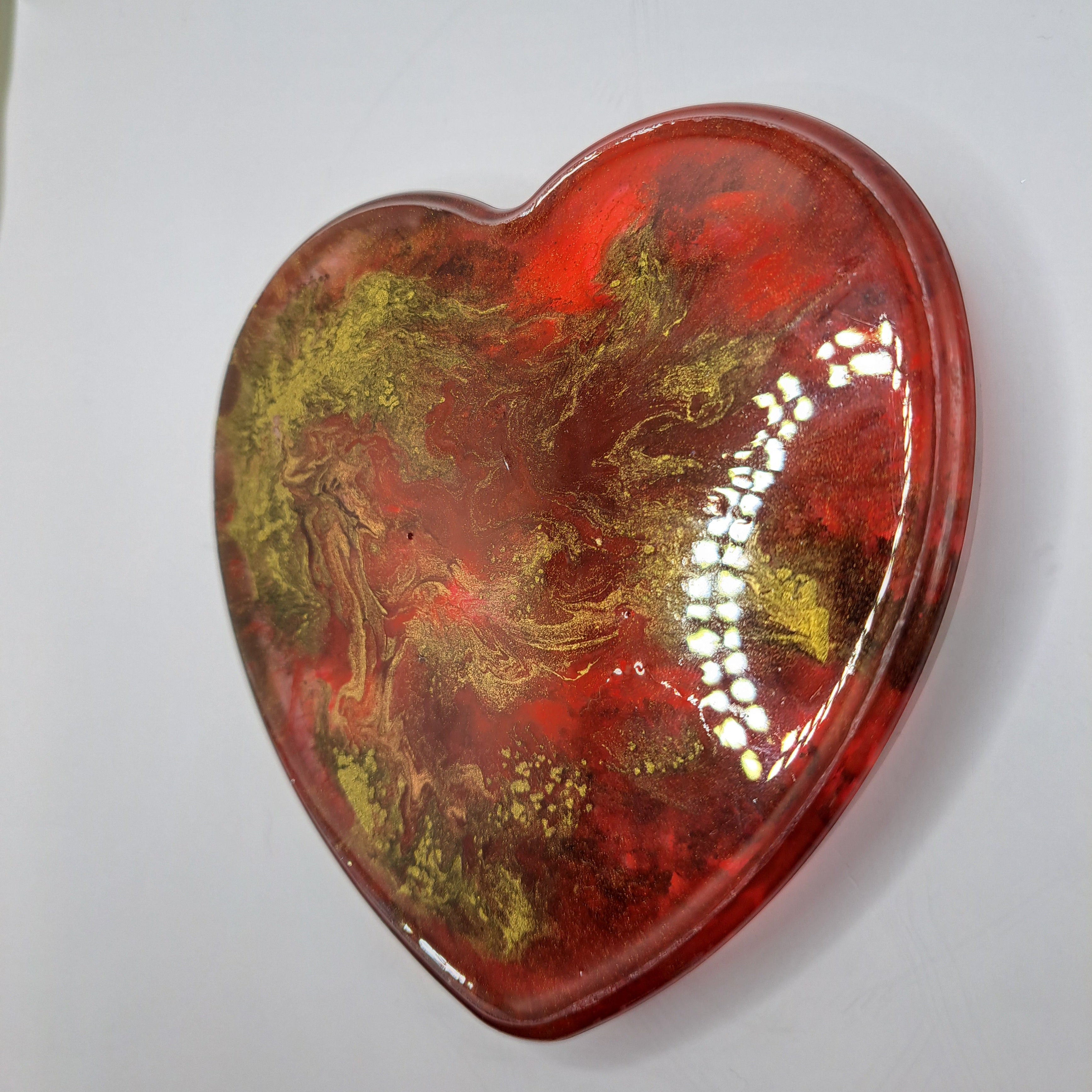Heart-shaped object with red and gold marbled pattern on a white background